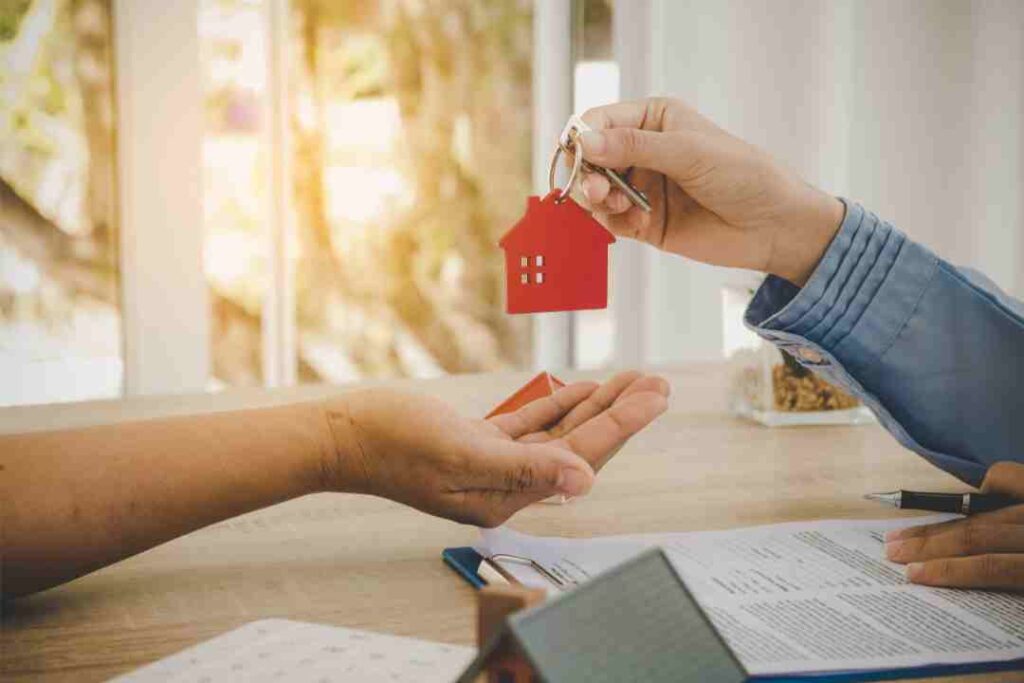 Hands exchanging house keys with a red keyring over a contract.